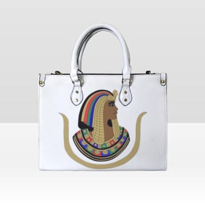 May include: White leather tote bag with a gold zipper and a colorful illustration of an Egyptian queen with a gold crown and a colorful necklace.
