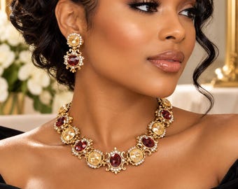 May include: A gold-toned necklace and matching drop earring set featuring alternating oval-shaped deep red and champagne-colored faceted crystals. Each crystal is surrounded by a decorative gold metal frame with small clear accent stones.