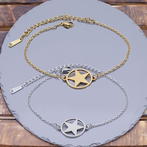 May include: Two gold and silver chain bracelets with star charms. The gold bracelet has a larger star charm and the silver bracelet has a smaller star charm.