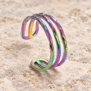 May include: An open-style ring featuring three parallel bands with a hammered, textured surface. The metal displays a vibrant, iridescent rainbow finish with shifting hues of purple, blue, green, and yellow across the entire structure.
