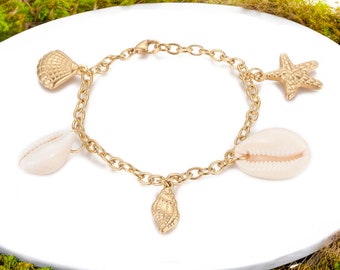 May include: Gold chain bracelet with five charms: a starfish, a seashell, and three smaller seashells. The bracelet is on a white surface.