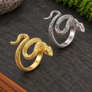 May include: Two rings shaped like coiled snakes, one finished in a bright gold tone and the other in an oxidized silver tone. Both rings feature detailed scale textures across the entire body and head of the snake, with a wrap-around design.