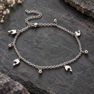 May include: A silver-toned metal chain anklet featuring alternating charms of small dolphins and smooth spherical beads. The jewelry piece includes a delicate link chain with a lobster claw clasp and an adjustable extension chain for a secure fit.