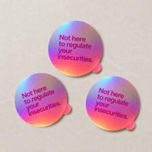 Op de afbeelding: Drie ronde stickers met een levendige holografische gradiëntachtergrond die verloopt van blauw naar paars en oranje. Elke sticker bevat de donkerroze tekst: Not here to regulate your insecurities. Elke sticker heeft een klein lipje.