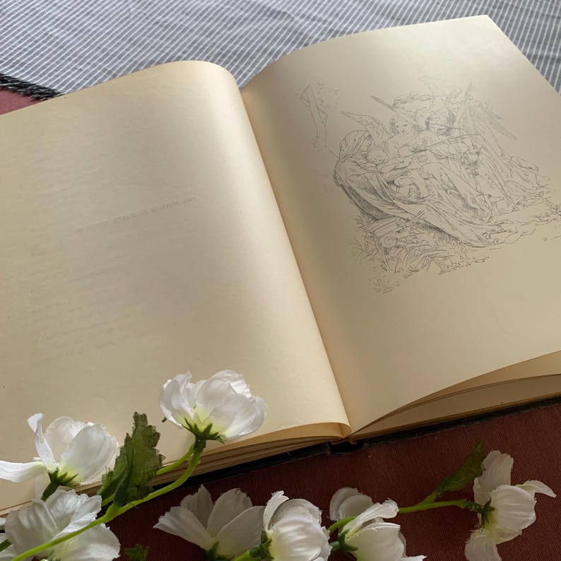 Peut inclure: Un livre ouvert avec un dessin au crayon d'un groupe d'anges sur la page de droite. La page de gauche est vide. Des fleurs blanches sont au premier plan.