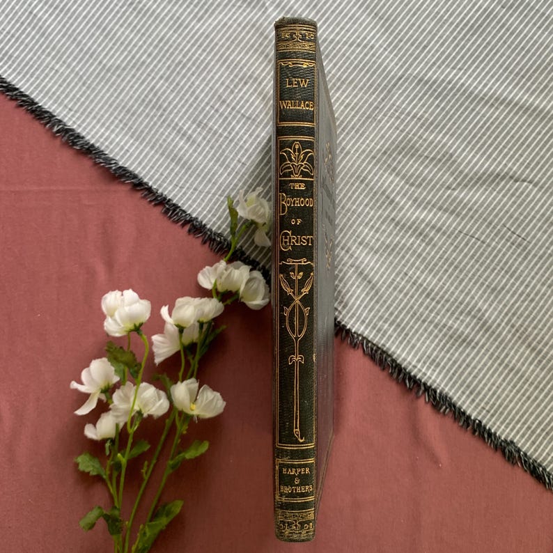 Peut inclure: Le dos d'un livre reli&eacute; noir avec des lettres dor&eacute;es. Le titre est "The Boyhood of Christ" par Lew Wallace. Le livre est publi&eacute; par Harper & Brothers.