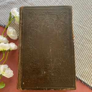 May include: A vintage, dark brown leather-bound book with intricate embossed floral designs on the cover. The book is slightly worn and shows signs of age.