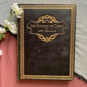 Peut inclure: Un livre reli&eacute; en cuir noir avec des lettres dor&eacute;es et une bordure d&eacute;corative. Le titre est "The Boyhood of Christ" par Lew Wallace.
