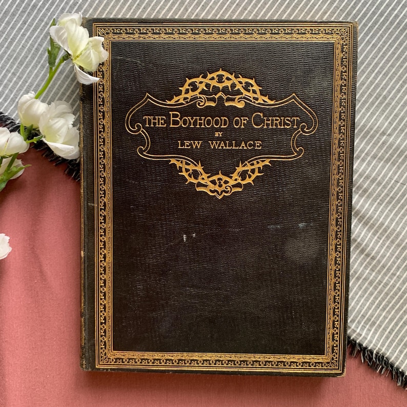 Peut inclure: Un livre reli&eacute; en cuir noir avec des lettres dor&eacute;es et une bordure d&eacute;corative. Le titre est "The Boyhood of Christ" par Lew Wallace.