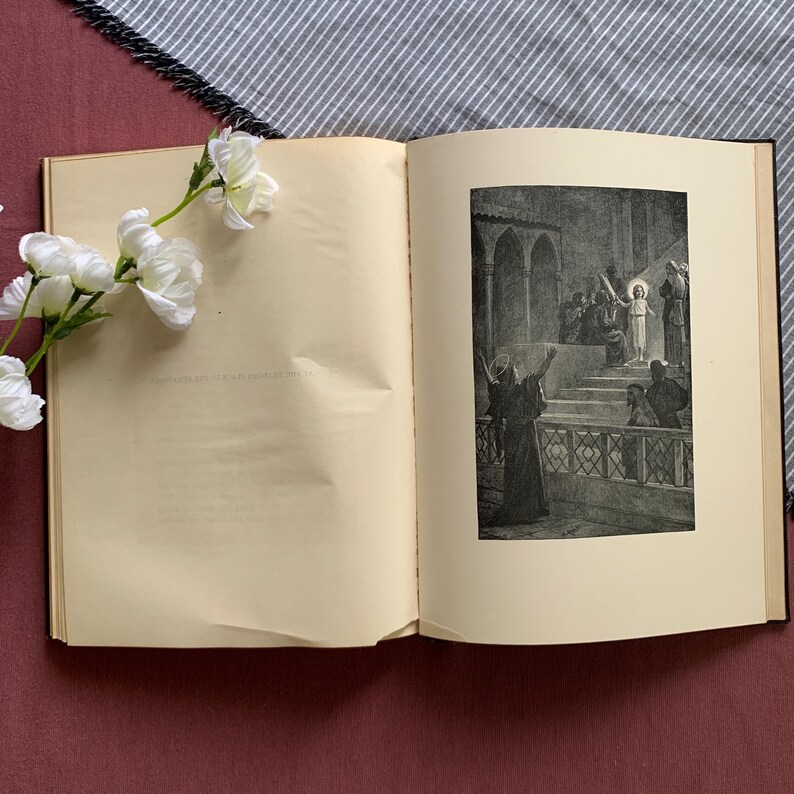Peut inclure: Un livre ouvert avec une illustration en noir et blanc d'une sc&egrave;ne religieuse. L'illustration repr&eacute;sente une figure en robe blanche debout sur une estrade entour&eacute;e d'autres figures. Le livre est ouvert &agrave; une page avec le texte "Et quand il eut dit ces paroles, il fut &eacute;lev&eacute; au ciel, et une nu&eacute;e le d&eacute;roba &agrave; leurs regards."