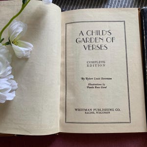 Pu&ograve; includere: Libro aperto intitolato "A Child's Garden of Verses" di Robert Louis Stevenson. L'edizione completa &egrave; pubblicata da Whitman Publishing Co. a Racine, Wisconsin. Fiori bianchi nell'angolo in alto a sinistra.