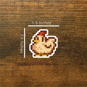 May include: A pixelated sticker of a brown and yellow chicken with a red comb, measuring 1.5 inches by 1.5 inches.