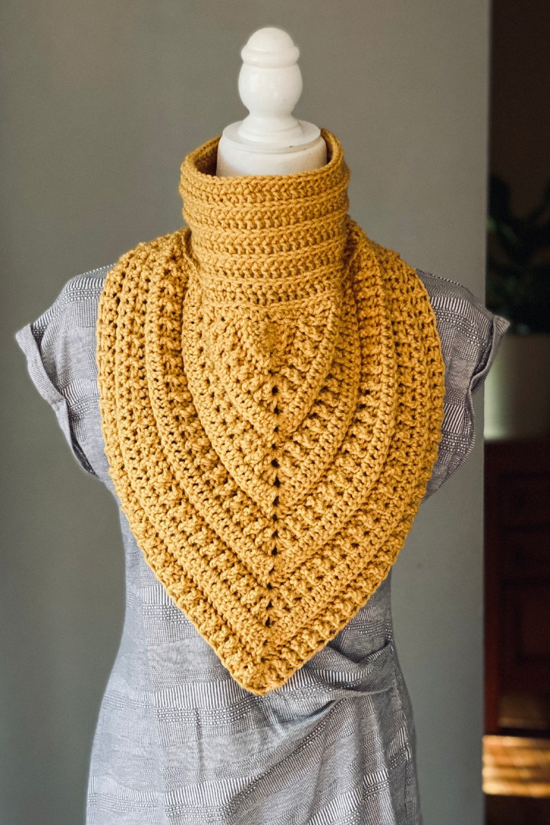 May include: A mustard yellow crocheted cowl neck scarf with a triangular shape.