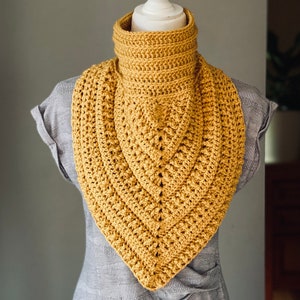 May include: A crocheted cowl in a mustard yellow colour. The cowl is made with a simple stitch pattern and has a triangular shape.
