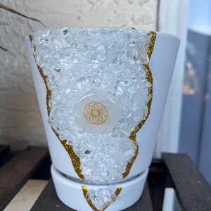 May include: White ceramic planter with a gold glitter rim and clear quartz crystals embedded in the side. A gold geometric design is visible on a white circle in the center of the planter.