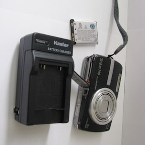 May include: A black Kastar battery charger, a silver and black rectangular battery, and a black Olympus Stylus 740 all-weather digital camera with a silver lens and a black wrist strap. The camera features the text Stylus 740 on the front.