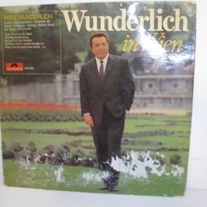 May include: Vintage vinyl record album cover featuring Fritz Wunderlich in Vienna. The cover has a photo of a man in a suit standing in a garden. The album title is in large yellow letters. The album cover has a green and white background.