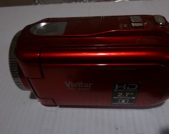 May include: A red Vivitar camcorder with a 2.7" HD screen. The camcorder has a silver microphone and a silver zoom control knob.