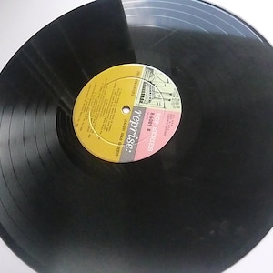 Puede incluir: Disco de vinilo negro con una etiqueta amarilla y rosa. La etiqueta tiene el texto "Pop Series" y "Reprise" con el número "R-4689" impreso en ella.