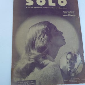 May include: A vintage sheet music cover for the song "Solo" by Herb Mendel and Buddy Morrow. The cover features a black and white photo of a woman with long hair looking up and a smaller photo of a man in a suit holding a microphone.
