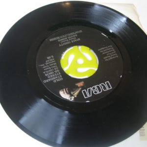 May include: A black vinyl record featuring the song "Space Oddity" by David Bowie. The record has a yellow and white label with the RCA logo. The record is a Gold Standard Stereo pressing.