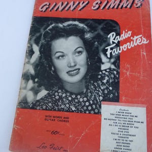 May include: A vintage sheet music cover featuring a black and white photo of Ginny Simms, a singer, with the title "Ginny Simms Radio Favorites" in red and white text. The cover also includes a list of songs with guitar chords.