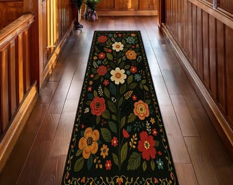 Può includere: Un tappeto runner nero con un design floreale. Il tappeto presenta un motivo floreale centrale con fiori rossi, arancioni e color crema, foglie verdi e un bordo dorato. Il tappeto è posto su un pavimento in legno in un corridoio.