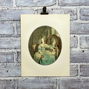 May include: A vintage print of a woman in a blue and white dress sitting in a chair and looking at her reflection in a mirror. The woman is holding a bouquet of flowers.