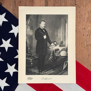May include: A black and white photograph of Ulysses S. Grant, the 18th President of the United States. The image shows Grant standing in front of a desk with a globe and other objects on it. The photograph is signed "U.S. Grant".