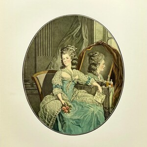 May include: A woman in a blue and white dress sits in a chair, holding a bouquet of pink roses. She is looking at her reflection in a mirror, which is behind her. The mirror is framed in wood and has a red velvet backing. The woman's reflection is wearing a similar dress and has her hair styled in a similar way.