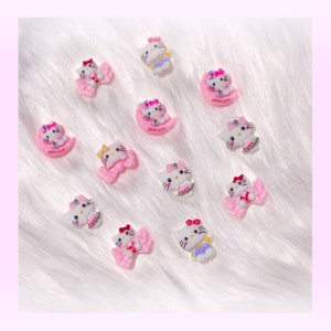 May include: Assortment of Hello Kitty charms featuring Hello Kitty in various poses, including wearing a dress, a bow, and a moon. The charms are made of white plastic with pink, purple, and blue accents.