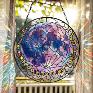 Pu&ograve; includere: Una vetrata rotonda con un design lunare nei toni del blu e del viola, con una rete di linee. Le parole "COPY MOON JOY" sono disposte attorno alla luna. La finestra &egrave; incorniciata con una cornice di metallo nero e una catena.