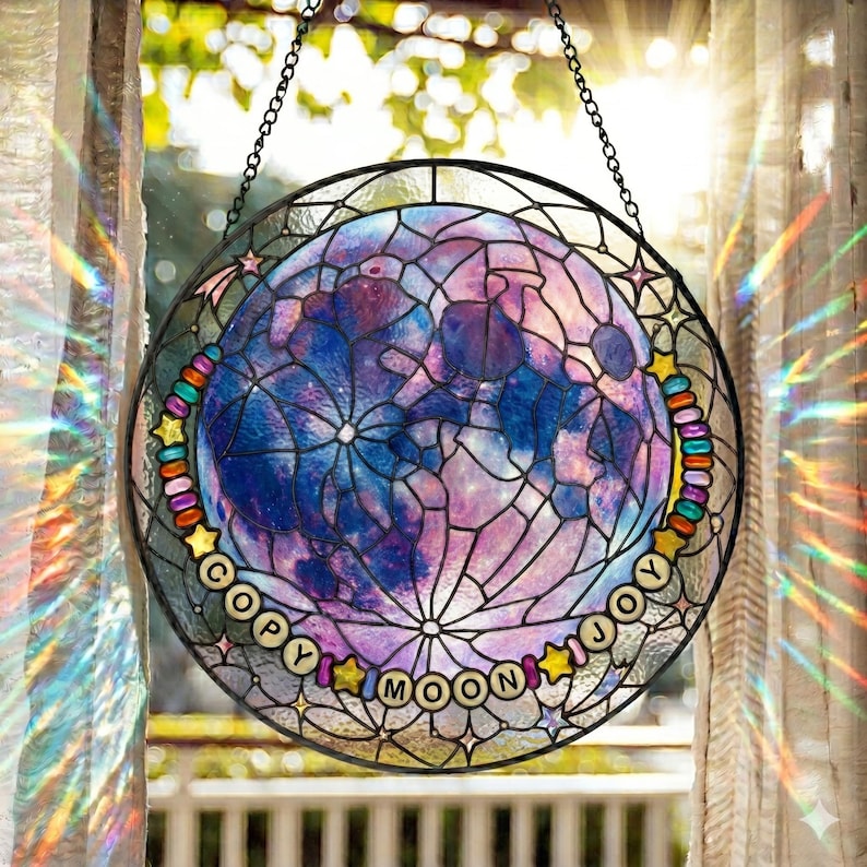 Pu&ograve; includere: Una vetrata rotonda con un design lunare nei toni del blu e del viola, con una rete di linee. Le parole "COPY MOON JOY" sono disposte attorno alla luna. La finestra &egrave; incorniciata con una cornice di metallo nero e una catena.