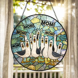 May include: Round stained glass window art featuring a flock of cartoon seagulls with open beaks, each shouting "MOM!" in black text. The birds have white bodies, gray wings, and yellow feet. The background is a mosaic of blue, green, and yellow glass.