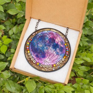 Pu&ograve; includere: Un pezzo rotondo di vetro colorato raffigurante una luna colorata nelle tonalit&agrave; del blu, viola e rosa. Il vetro &egrave; incorniciato in un bordo marrone scuro con le parole "COPY MOON JOY" in un carattere colorato. Il pezzo &egrave; esposto in una scatola di cartone.