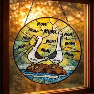 May include: Round stained glass window with a seagull design. The seagulls are white with black accents, standing on a rock above blue water. The word "MOM!" is repeated around the seagulls. The names "Sophia" and "James" are below the seagulls.