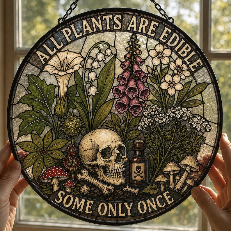 May include: Round stained glass art piece with the text "ALL PLANTS ARE EDIBLE SOME ONLY ONCE". The artwork features a skull, bones, mushrooms, and various plants in shades of green, purple, and white. A small bottle with a skull and crossbones is also visible.