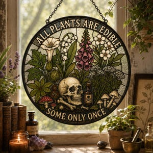 May include: A round stained glass window with a black border and chain. The design features a skull, mushrooms, and various plants, with the text "ALL PLANTS ARE EDIBLE SOME ONLY ONCE".