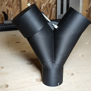 May include: A black plastic 3D printed Y-shaped connector with two round openings at the top and one round opening at the bottom.