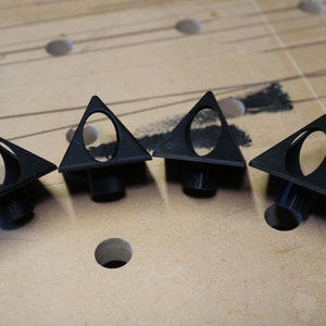 May include: Four black triangular-shaped plastic pieces with a circular hole in the center. The pieces are arranged in a row on a light brown surface.