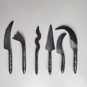 Può includere: Sei diversi utensili in metallo con forme e design unici. Gli utensili sono tutti in metallo scuro e hanno una punta affilata a un'estremità.