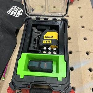 May include: A black and red Milwaukee Packout storage case with a clear lid, containing a yellow and black DeWalt laser tool, six AA batteries, and a green 3D-printed insert holding a small dark green Bosch pouch with a black strap and buckle.