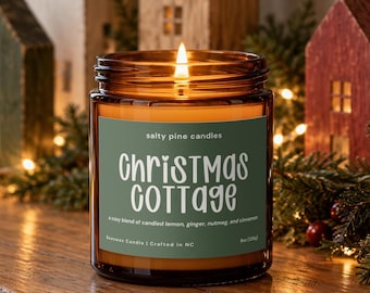May include: A lit candle in an amber glass jar with a green label. The label reads Salty Pine Candles, Christmas Cottage, a cozy blend of candied lemon, ginger, nutmeg, and cinnamon, Beeswax Candle | Crafted in NC, 8oz (226g).