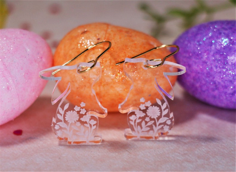 K&ouml;nnte beinhalten: Ein Paar transparente Acryl-Ohrringe in Form von Hasen mit Blumenmustern. Die Ohrringe haben goldene Haken.