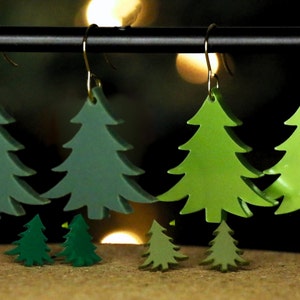 May include: A set of five green Christmas tree earrings. The earrings are made of acrylic and have a shiny finish. The earrings are in different sizes, with the largest being about 3 inches tall.