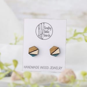 May include: A pair of hexagonal wooden earrings with a geometric design in shades of brown, white, and blue. The earrings are displayed on a white card with the text "Crafty Little Birch" and "Handmade Wood Jewelry".