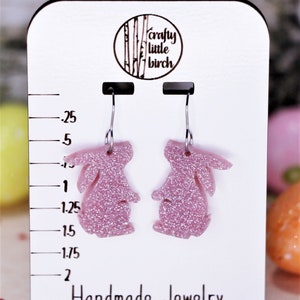 K&ouml;nnte beinhalten: Ein Paar rosa glitzernde Hasen-Ohrringe an einer wei&szlig;en Displaykarte mit dem Text "crafty little birch" und "Handmade Jewelry".