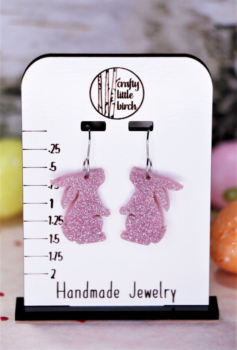 K&ouml;nnte beinhalten: Ein Paar rosa glitzernde Hasen-Ohrringe an einer wei&szlig;en Displaykarte mit dem Text "crafty little birch" und "Handmade Jewelry".