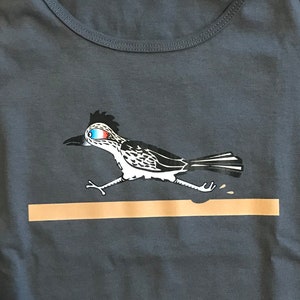 May include: A dark blue tank top with a white and black illustration of a roadrunner running across a brown stripe. The roadrunner has a blue and red eye.