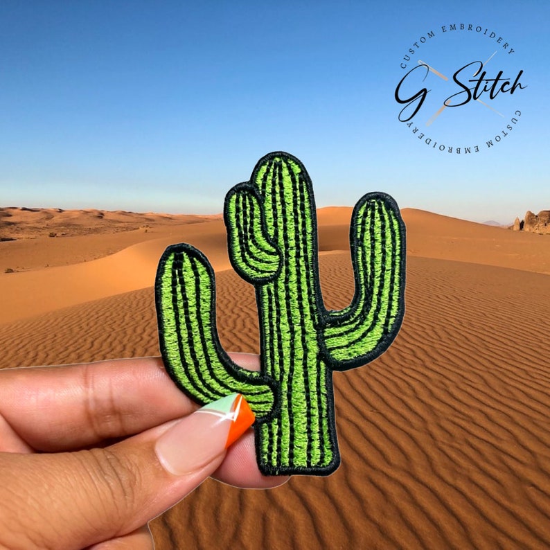Puede incluir: Un parche de cactus verde con costuras negras, frente a un paisaje des&eacute;rtico. El parche presenta el texto "Custom Embroidery G Stitch Custom Embroidery" en un dise&ntilde;o circular.